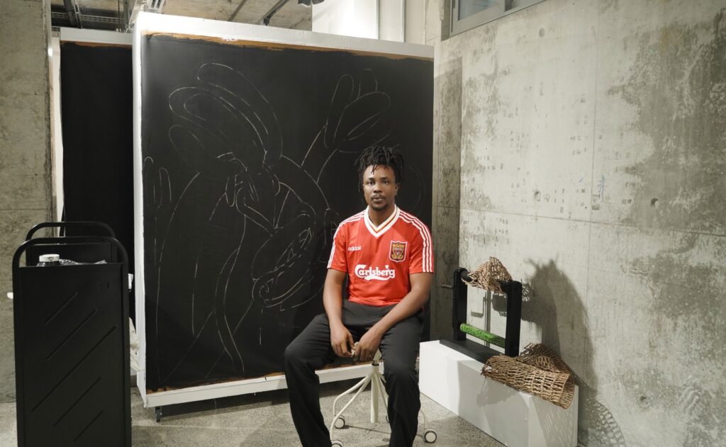 Jonathan sitting on a stool with work behind him at G.A.S residency