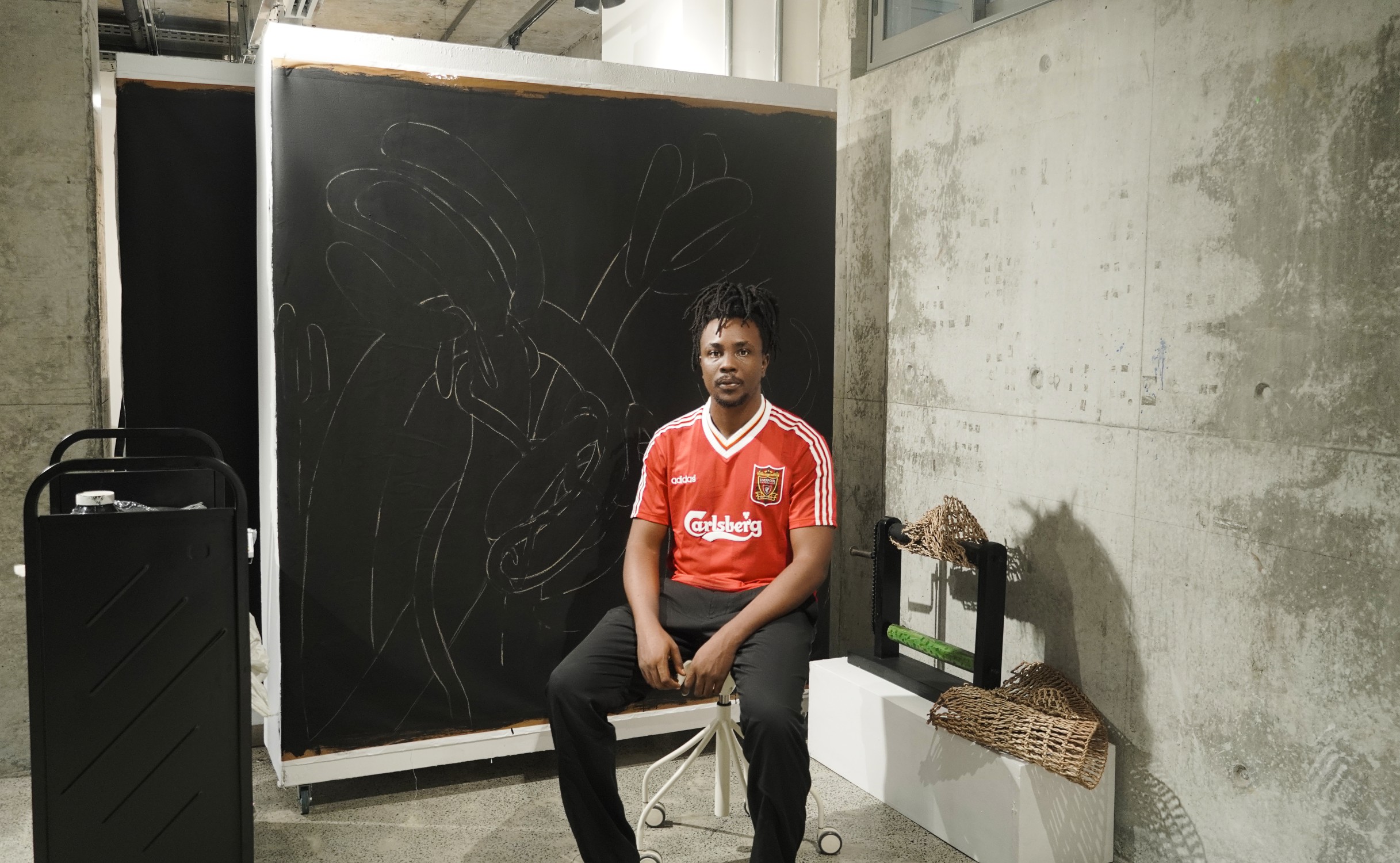Jonathan sitting on a stool with work behind him at G.A.S residency